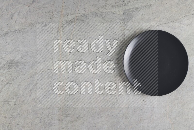 A black ceramic circular plate on grey marble background