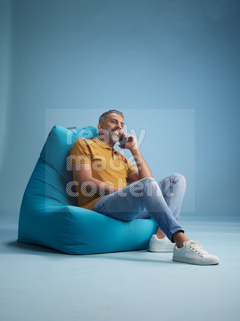 A man sitting on a blue beanbag and talking on the phone