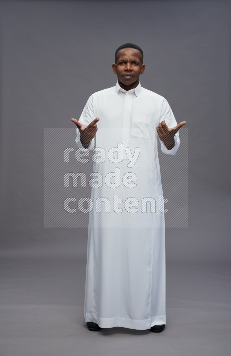 Saudi man wearing thob standing interacting with the camera on gray background