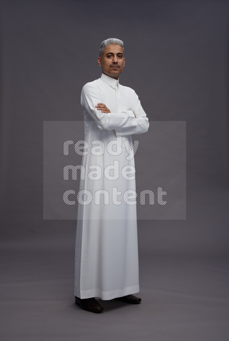 Saudi man wearing thob standing with crossed arms on gray background