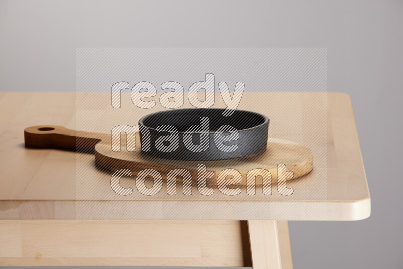 black bowl placed on a  wooden oval cutting board on the edge of wooden table