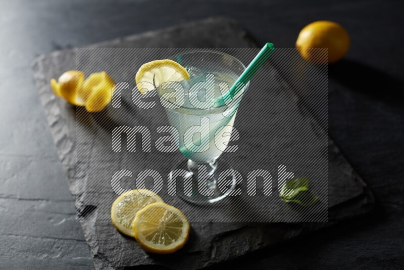 A glass of lemon juice with a straw on black background