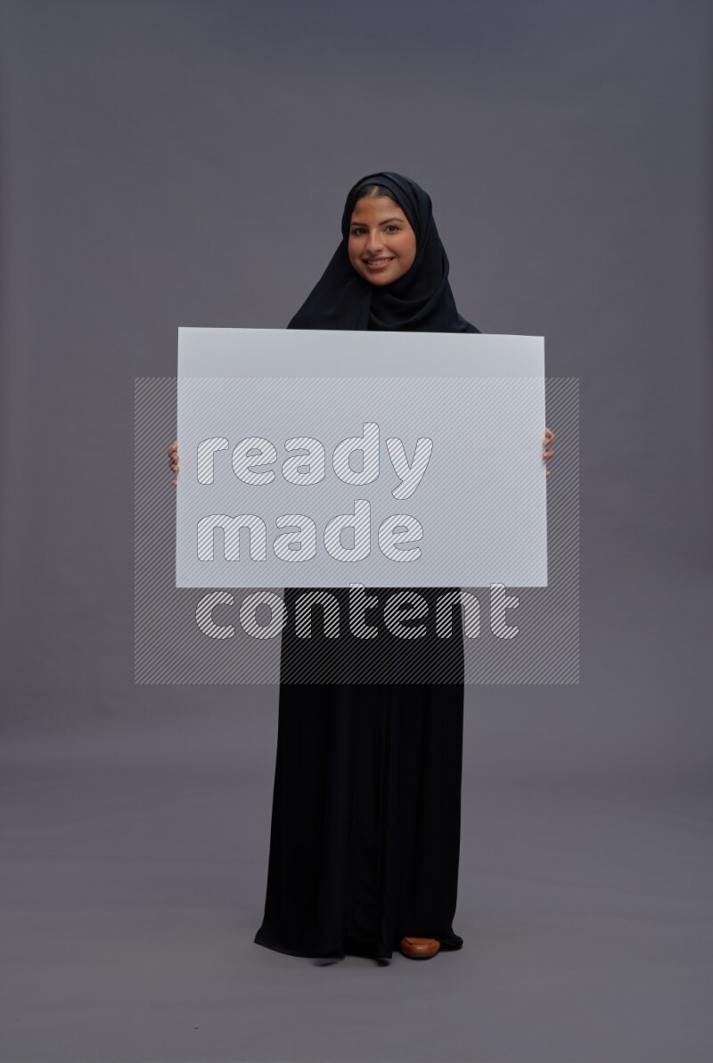 Saudi woman wearing Abaya standing holding white board on gray background