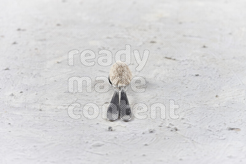 ملعقتان معدنيتان أحدهما ممتلئة ببودرة البصل علي خلفية بيضاء