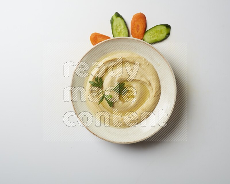 Hummus in a pottry plate garnished with parsley on a white back ground