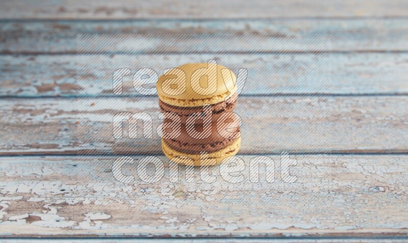 45º Shot of two Yellow and Brown Chai Latte macarons on light blue wooden background