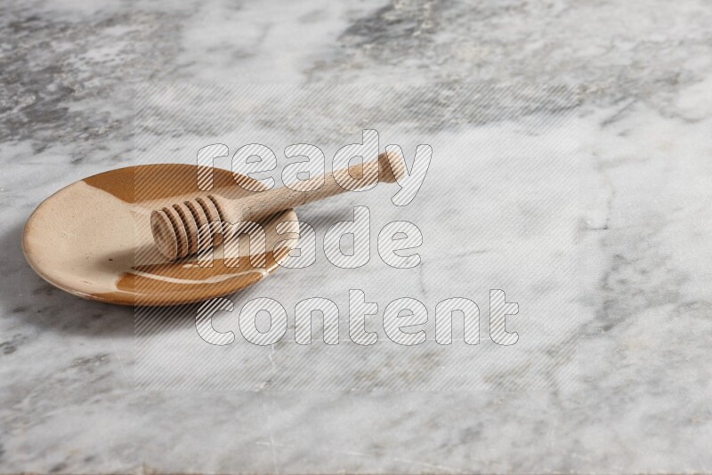 Multicolored pottery plate with wooden honey dipper in it on grey marble background