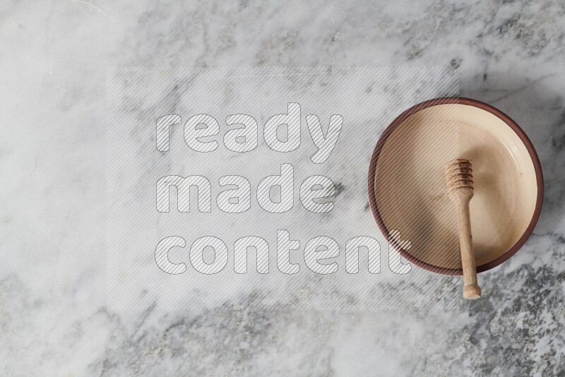 Beige pottery oven plate with wooden honey dipper in it on grey marble background