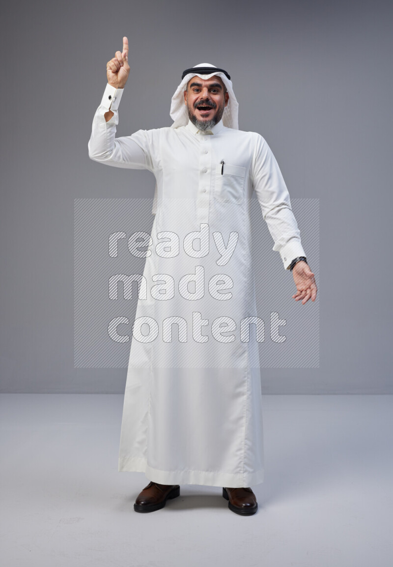 Saudi man Wearing Thob and white Shomag standing interacting with the camera on Gray background