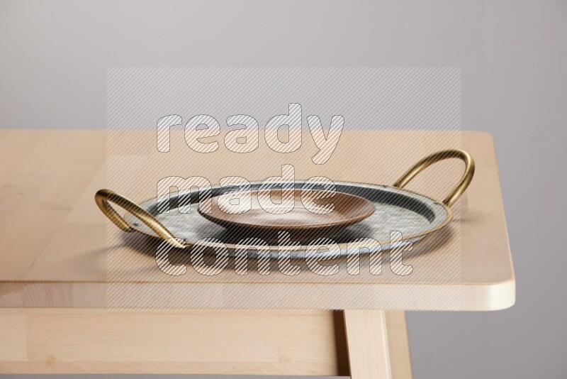 multicolored plate placed on a rounded stainless steel tray with golden handels on the edge of wooden table