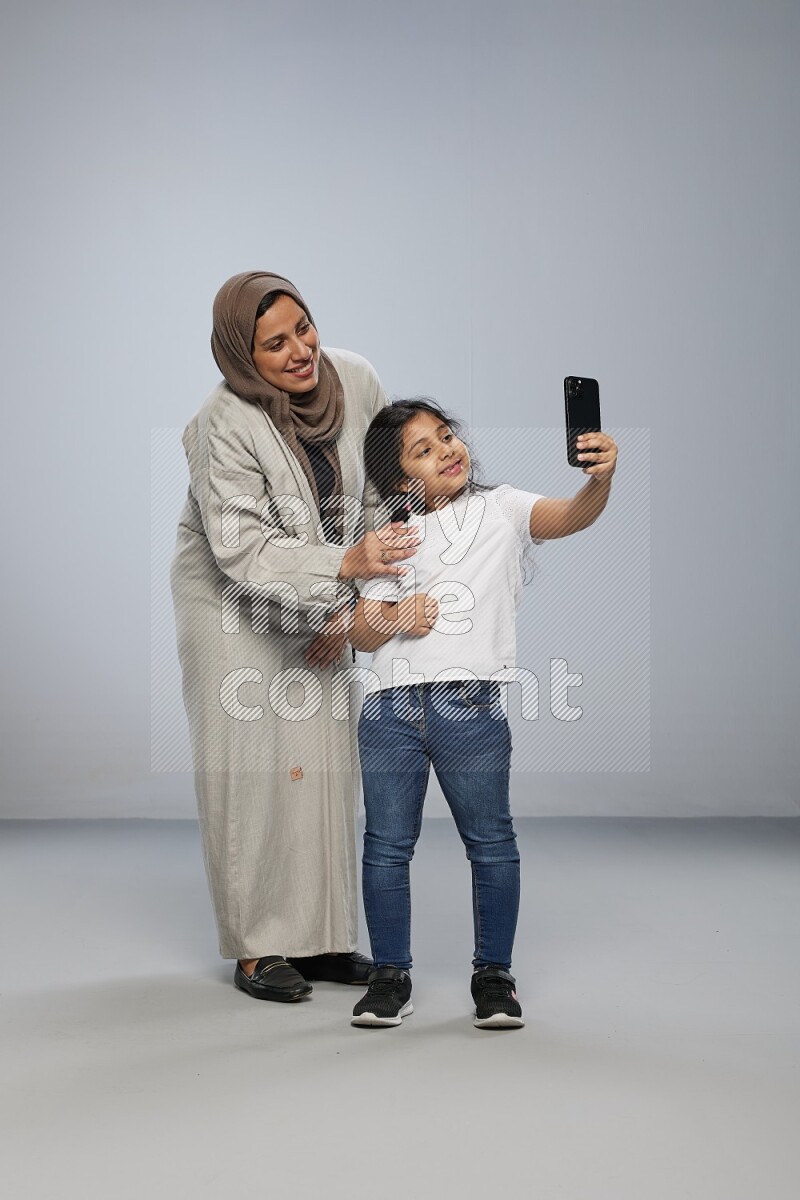 A girl standing taking selfie with her mother on gray background