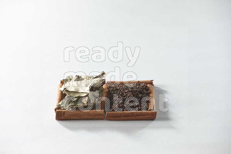 مربعان من أعواد القرفة ممتلئان بالقرنفل وأوراق الغار علي خلفية بيضاء