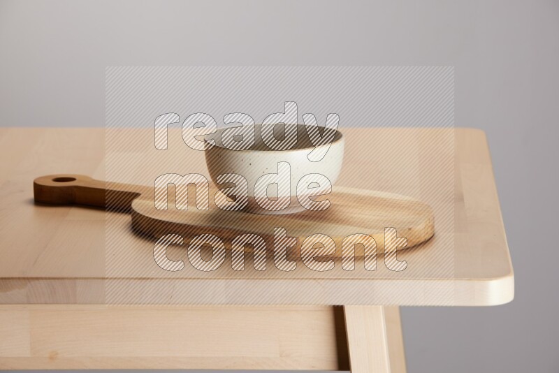 multi colored bowl placed on a  wooden oval cutting board on the edge of wooden table