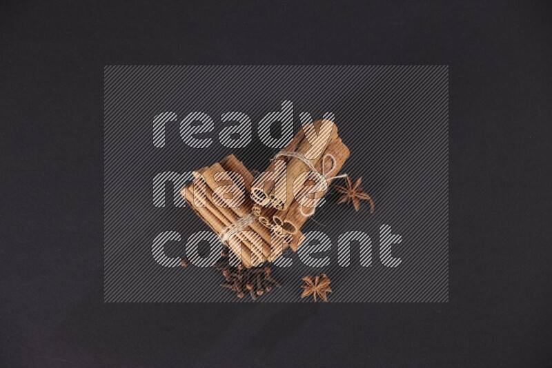 Two bounded stacks of cinnamon sticks with cloves and star anise on black background