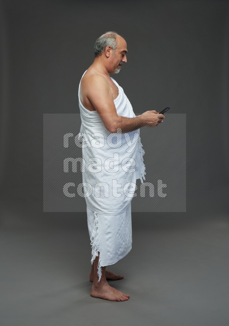 A man wearing Ehram Standing texting on phone on gray background