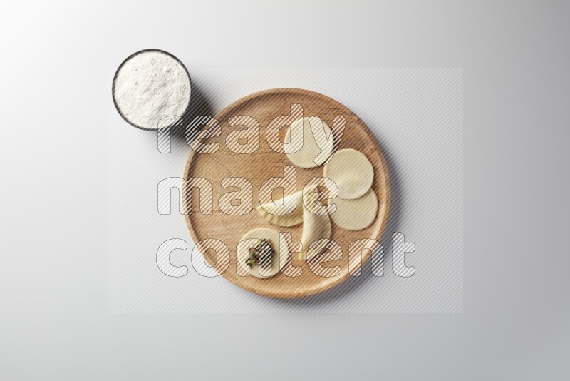 two closed sambosas and one open sambosa filled with meat while flour aside in a wooden dish on a white background