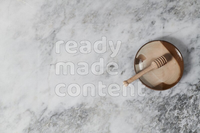 طبق فخاري متعدد الألوان مع ملعقة عسل خشبية بداخله على خلفية من الرخام الرمادي