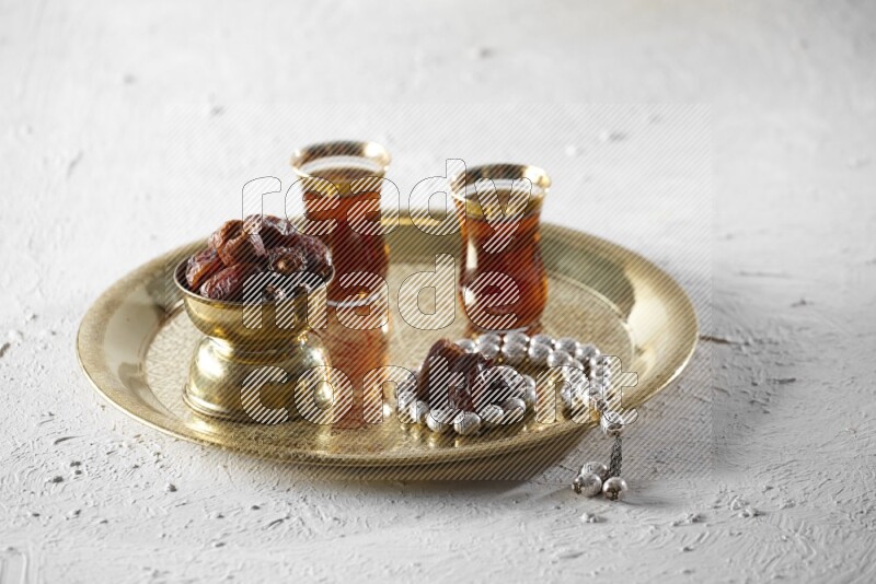 Dates in a metal bowl with tea and prayer beads on a tray in a light setup