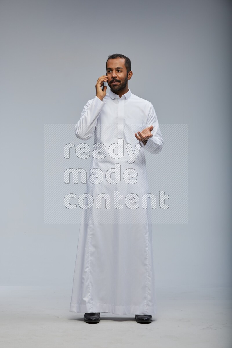 Saudi man wearing Thob standing talking on phone on Gray background