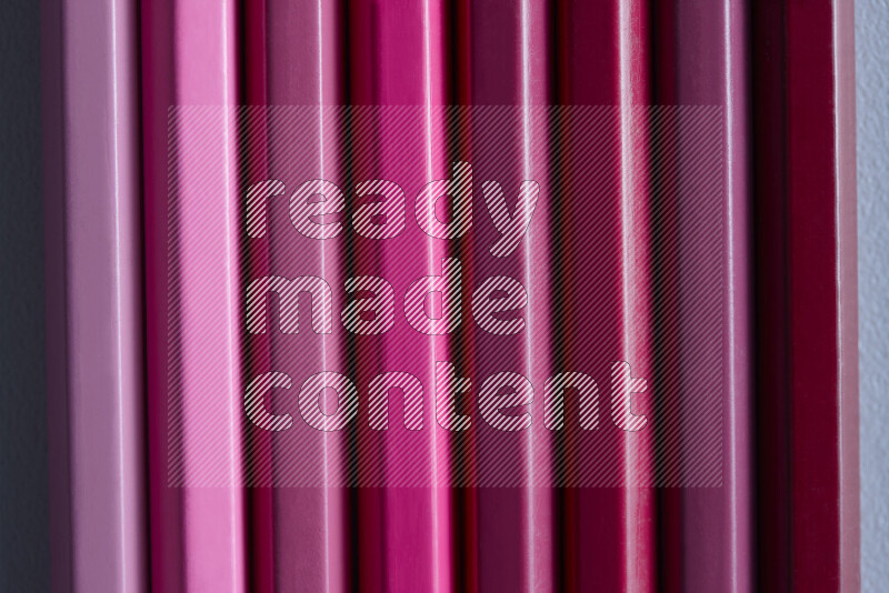 مجموعة من أقلام الرصاص الملونة مرتبة لتعرض تدرجا من الألوان الوردية علي خلفية رمادية