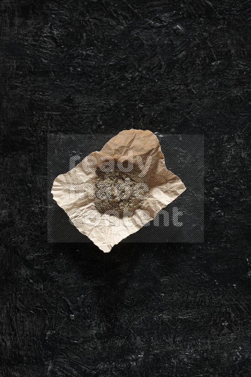 Cardamom powder in a crumpled piece of paper on textured black flooring