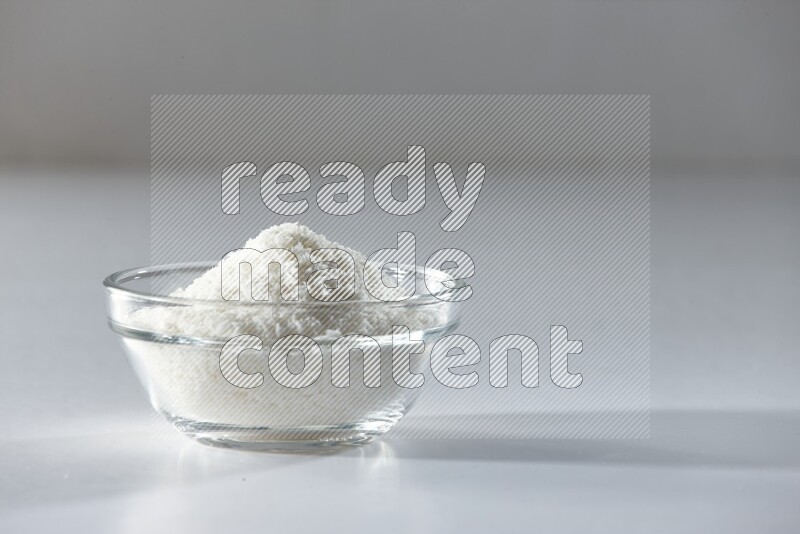 A glass bowl full of desiccated coconut on a white background in different angles