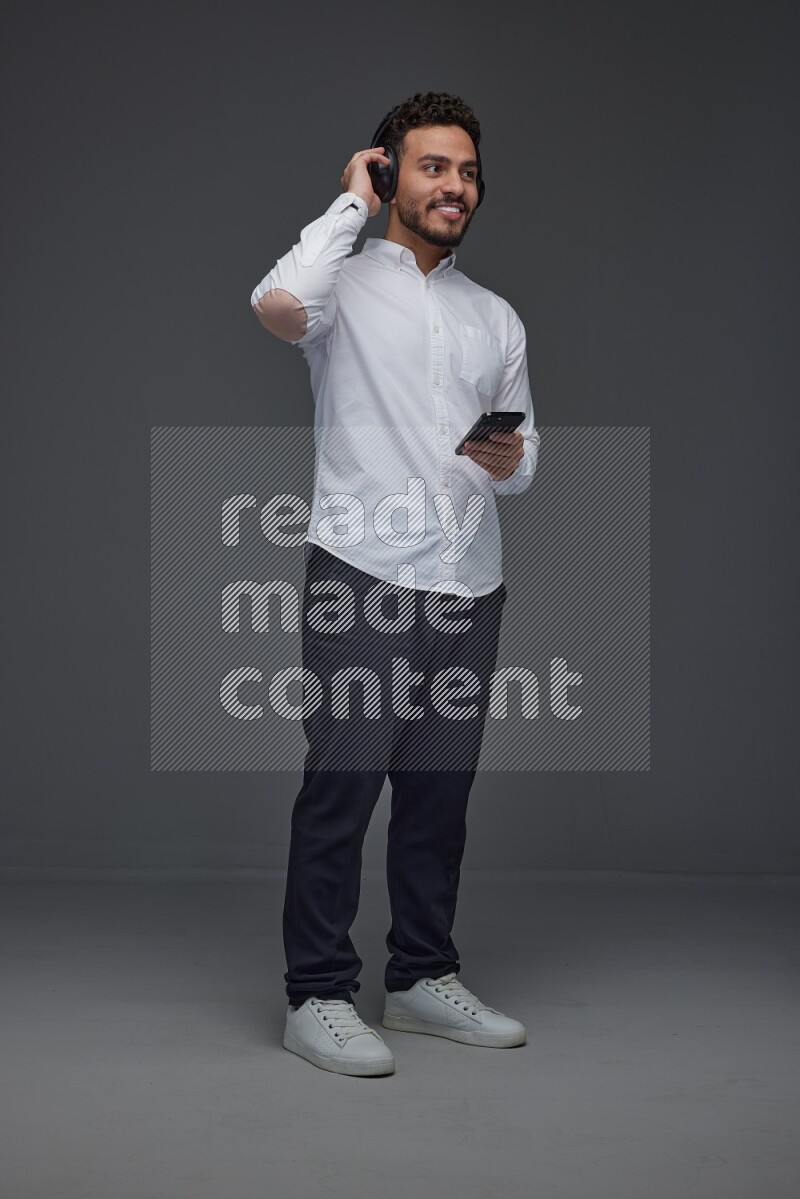 A man wearing smart casual and using his phone and headphone eye level on a gray background