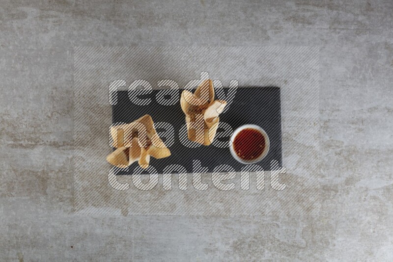 wonton cups with soy sauce ramkin on rectangle slate on grey textured counter top