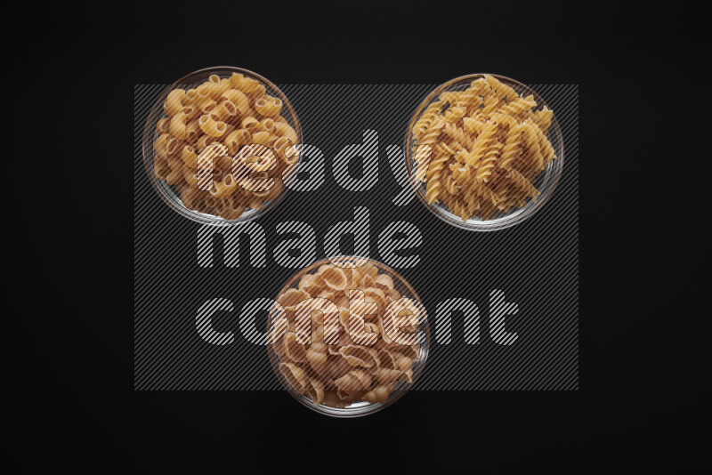 Different pasta types in glass bowls on black background