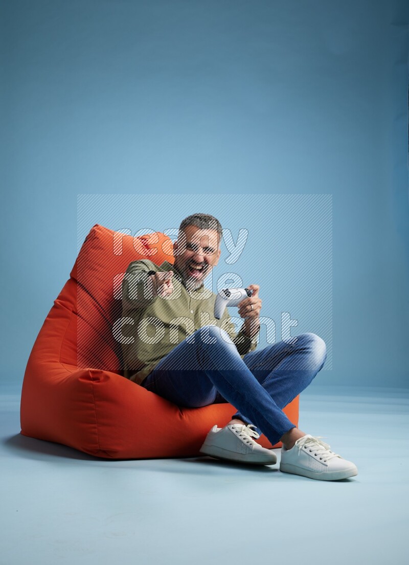 A man sitting on an orange beanbag and gaming with joystick