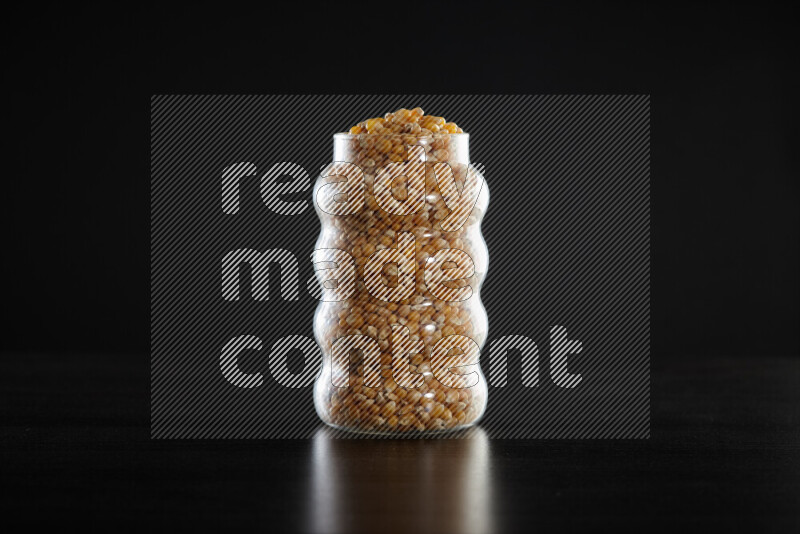 Dry corn kernels in a glass jar on black background