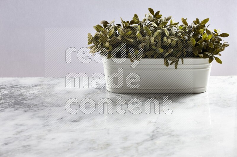 Multiple green artificial plants in white pot on grey marble background