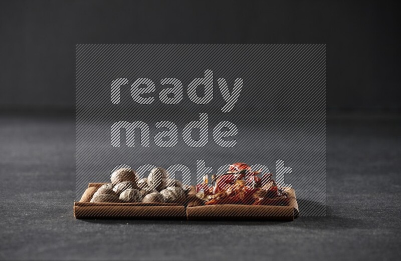 2 squares of cinnamon sticks full of nutmegs and dried red chilis on black flooring