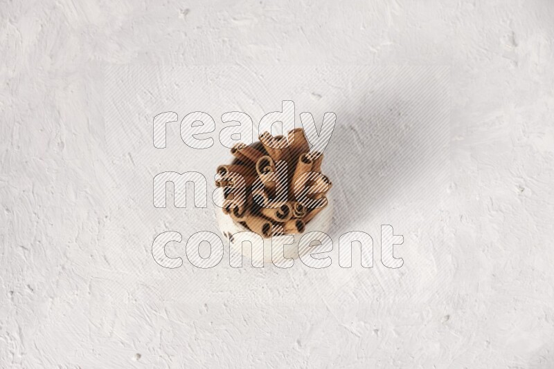 Cinnamon sticks in a beige bowl on a white background