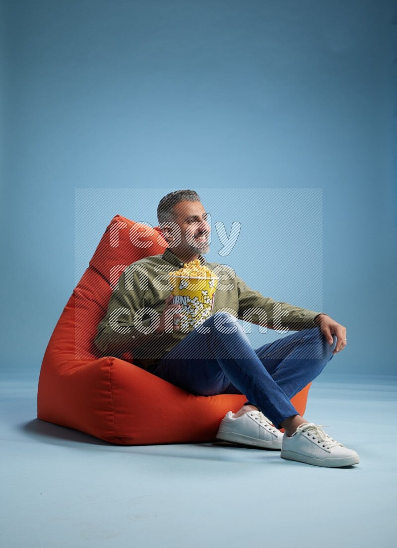 A man sitting on an orange beanbag and eating popcorn