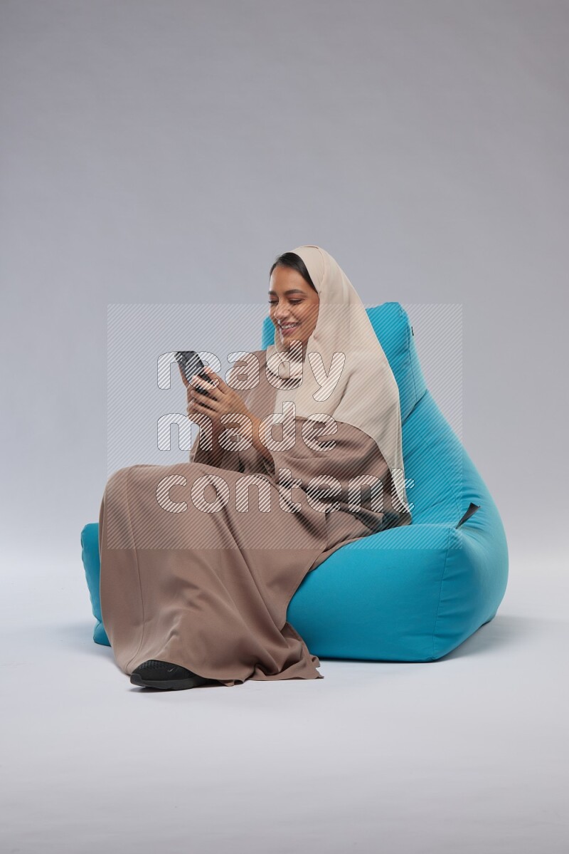 A Saudi woman sitting on a blue beanbag and texting on phone