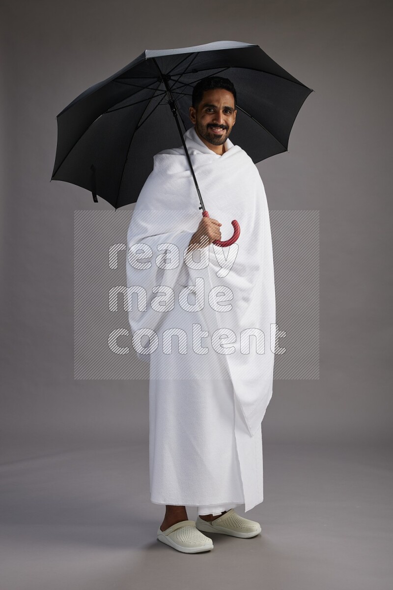 A man wearing Ehram Standing holding umbrella on gray background