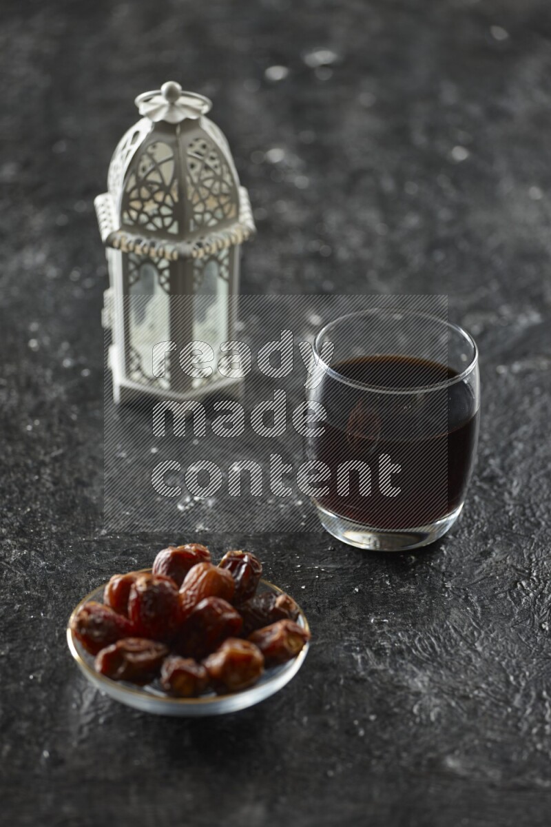 A white lantern with different drinks, dates, nuts, prayer beads and quran on textured black background