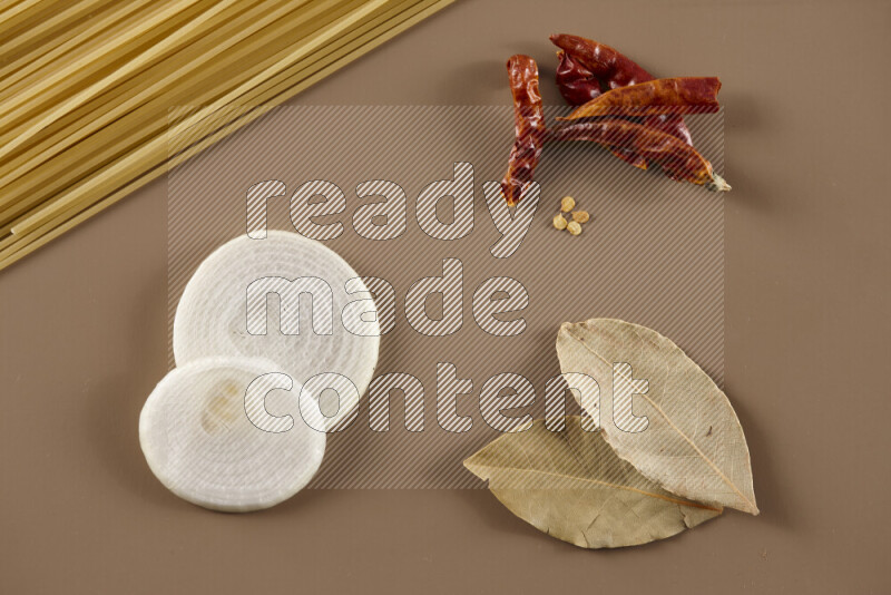 Raw pasta with different ingredients such as cherry tomatoes, garlic, onions, red chilis, black pepper, white pepper, bay laurel leaves, rosemary and cardamom on beige background