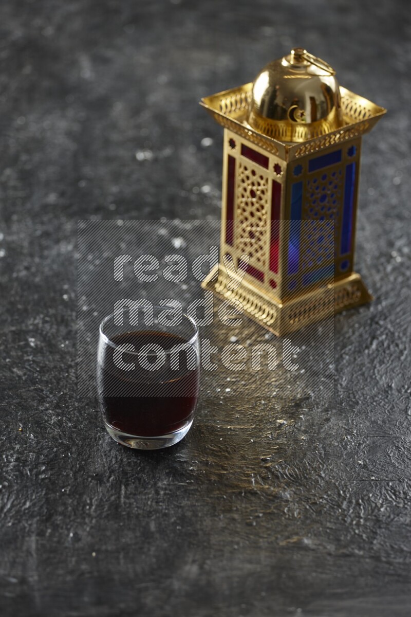 A golden lantern with different drinks, dates, nuts, prayer beads and quran on textured black background