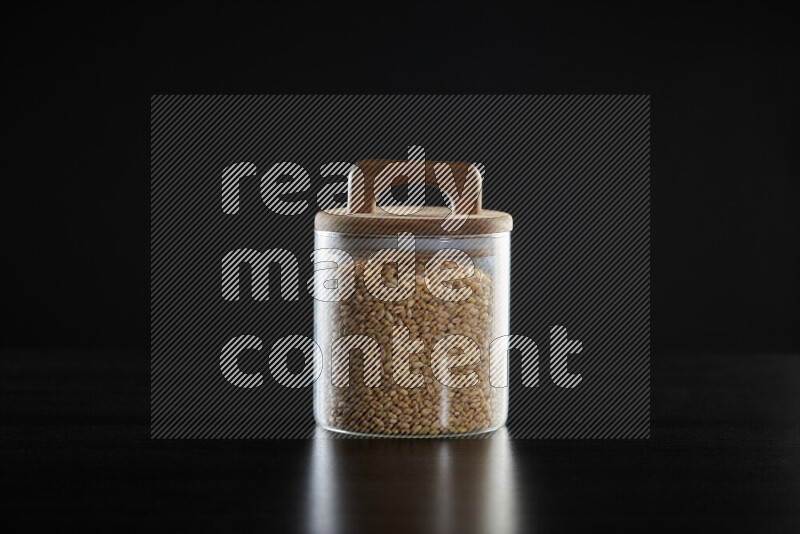 Hulled wheat in a glass jar on black background