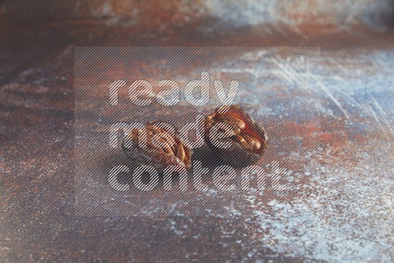 two pecan stuffed madjoul dates on a rustic reddish background