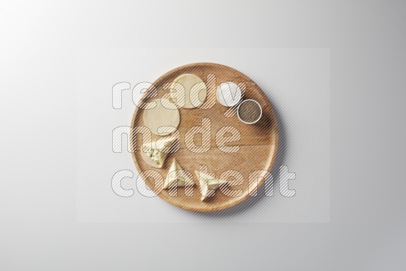two closed sambosas and one open sambosa filled with cheese while salt, and black pepper aside in a wooden dish on a white background