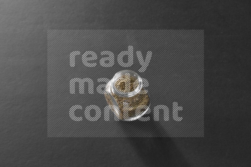 A glass spice jar full of cumin on black flooring