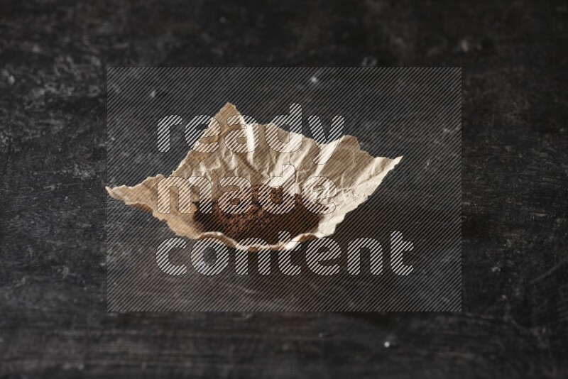 Cloves powder in crumpled piece of paper on a textured black flooring