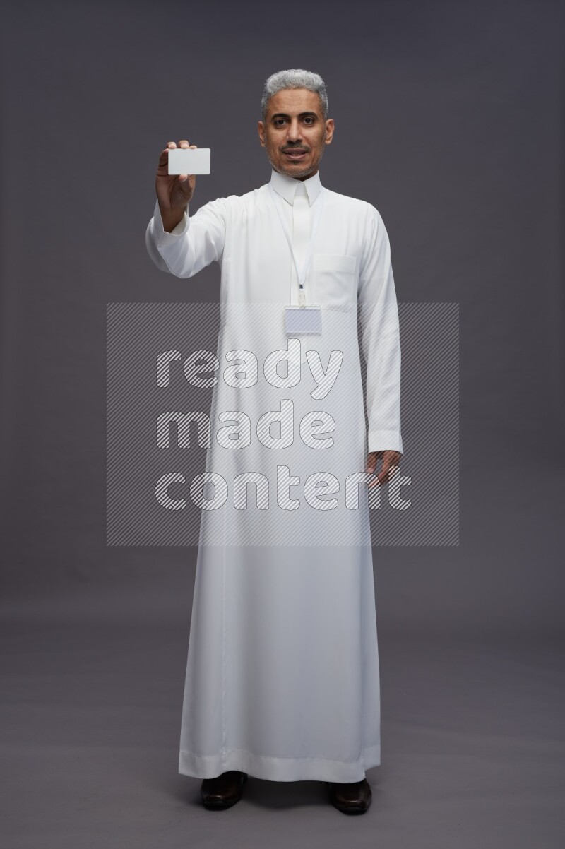 Saudi man wearing thob with neck strap employee badge standing holding ATM card on gray background