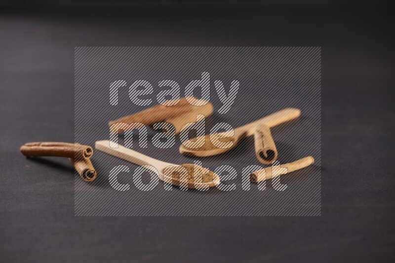 Two wooden spoons full of cinnamon powder with cinnamon sticks on black background