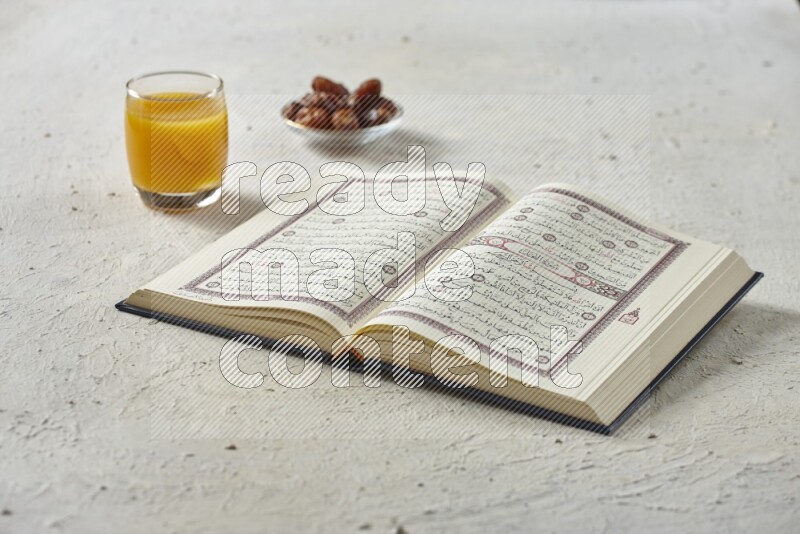 Quran with dates, prayer beads and different drinks all placed on textured white background