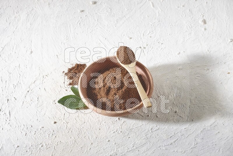 A wooden bowl and a wooden spoon full of cloves powder on a textured white flooring