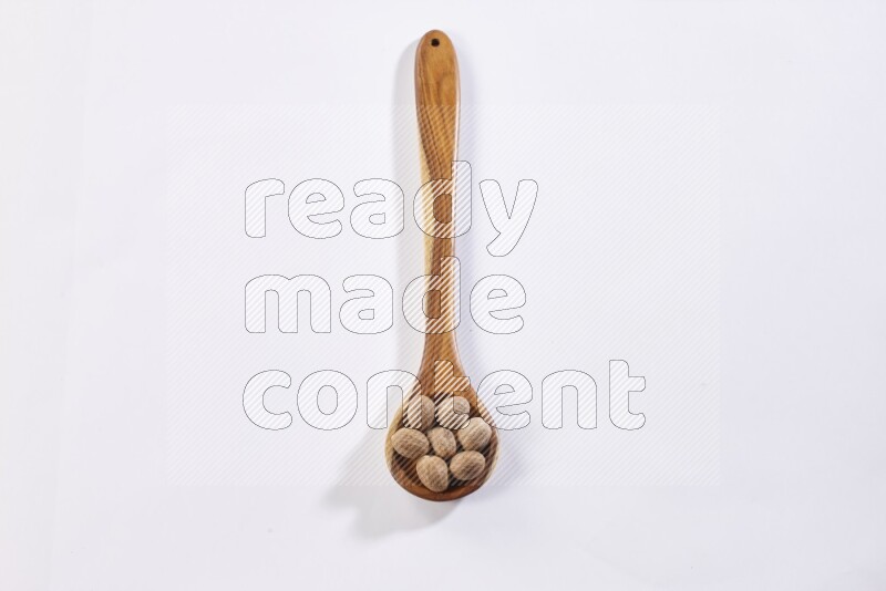 A wooden ladle full of whole nutmeg seeds on a white flooring